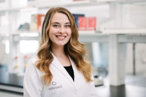 Sara Ord is Director of Species Restoration at Colossal. Her headshot in a white lab coat in a lab environment. 